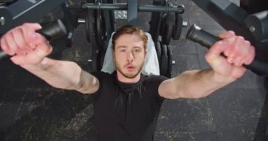 Lviv, Ukrane 04.28.2021: Güçlü adamın üst görünümü, kollarını spor salonunda çalıştırırken ve özel makinede güç eğitimi alırken ağır sıkmaktadır. Spor ve spor konsepti