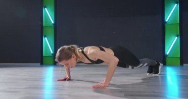 Spor. Genç atletik kadının, karanlık spor salonunda antrenman yaparken yerde şınav çekişini uzun uzun izlemek. Güçlü ve kaslı kız dikkatli egzersiz yapıyor.