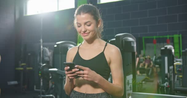 Låg vinkel syn på den starka idrottskvinna tittar på smartphone skärmen och meddelanden med någon efter träning. Idrott och fritid — Stockvideo