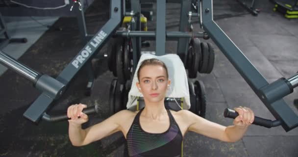 2021年4月28日:力強い女性のトップビューは、ジムで腕を訓練し、特別なマシンでパワートレーニングを受けながら、重い重量を圧迫します。スポーツとワークアウトのコンセプト — ストック動画