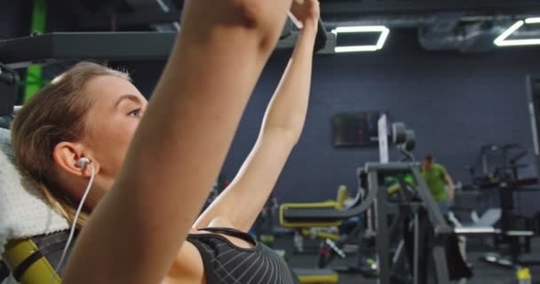 Vista recortada de la mujer fuerte aprieta el peso pesado y entrenar sus brazos en el gimnasio mientras tiene entrenamiento de fuerza en la máquina especial. Concepto de deporte y entrenamiento — Vídeos de Stock