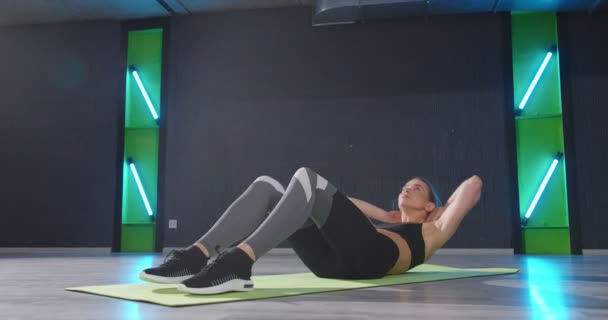 Pełna długość widok młodej zmęczonej kobiety w odzieży sportowej pompującej prasę podczas treningu w ciemnej siłowni. Sport i koncepcja zdrowego stylu życia — Wideo stockowe