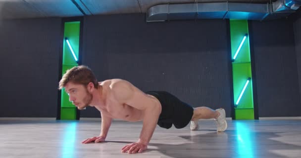 Full length view of the young athletic man doing push-ups of the floor while training at the dark gym. Muscular and strong guy exercising carefully. Sport — Stock Video
