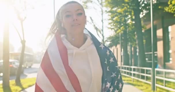 Nahaufnahme Porträt einer glücklichen jungen lächelnden schönen Frau aus dem Kaukasus, die Musik über Kopfhörer hört, während sie auf der Straße mit der US-Flagge läuft. Positive Sportlerin mit amerikanischer Flagge joggt draußen — Stockvideo