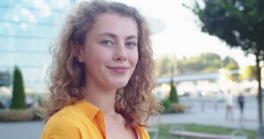 Kafkasyalı neşeli genç bir kadının iyi bir ruh hali içinde dikilip kameraya bakıp gülümseyen portresini yakından çek. Şehirde poz veren kıvırcık saçlı güzel, neşeli bir kadın. Duygular konsepti