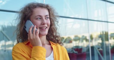 Şehirde caddede dururken gülümseyen ve cep telefonuyla konuşan mutlu beyaz kadın portresi. Neşeli kadın dışarıdaki akıllı telefondan arıyor. Pozitif ruh hali, konsepti ara.