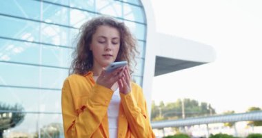 Kasabanın dışında duran ve akıllı telefondan sesli mesaj kaydeden güzel beyaz bir kadının portresi. Şehirde cep telefonu uygulaması kullanan güzel bir kadın. Şehir tarzı, teknoloji kavramı