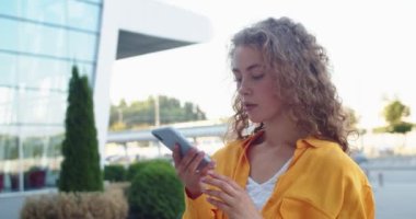 Genç, güzel, beyaz, mutlu bir kadın şehirde duruyor ve akıllı telefondan sesli mesaj yolluyor. Şehirdeki güzel bir kadın cep telefonu hoparlöründen konuşuyor. Portre, teknoloji konsepti