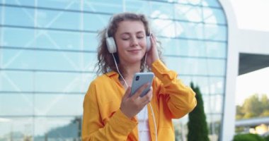Sokakta yürüyen ve akıllı telefon kullanarak kulaklıkla müzik dinleyen neşeli, genç, beyaz bir kadının portresini yakından çek. Mutlu kadın gülümsüyor akıllı telefondan gelen sesten keyif alıyor