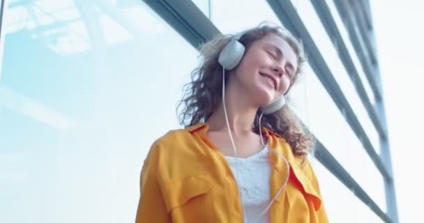 Gros plan de Caucasienne joyeuse jeune femme dansant en plein air en écoutant la chanson favori à l'extérieur. Belle femme avec le sourire sur le visage aime la musique debout dans la rue en ville. Loisirs, concept relax — Video