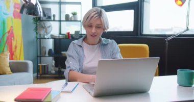 Beyaz, sarışın, güzel bir kadın dizüstü bilgisayarda çalışıyor. İnternette geziniyor. Evdeki dolapta otururken daktilo yazıyor.