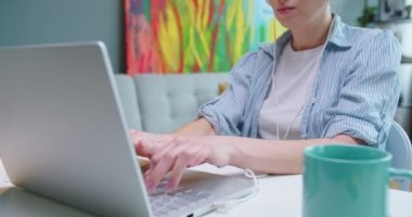 Oda dolabında otururken dizüstü bilgisayarla mesaj atan ve kulaklıkla müzik dinleyen beyaz kadın ellerini kapatın. Öğrenci öğrenimi, mesafe çalışması, ev, ofis, işçi konsepti