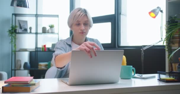 Portrét mladé bělošky sedící za stolem v místnosti a začít psát notebook a prohlížení on-line doma. Krásná pracovnice poklepávající na počítač ve skříni. Koncept úlohy — Stock video