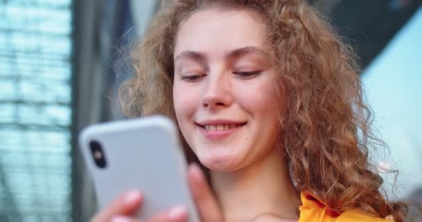 Close-up van Kaukasische vrolijke vrolijke vrouw tikken op smartphone buiten. Jonge mooie vrouw surfen online typen op mobiele telefoon op straat met een glimlach op het gezicht. Vrije tijd, communicatieconcept — Stockvideo