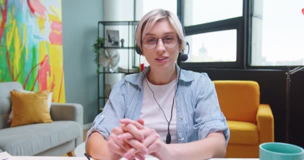 Close-up portret van gelukkige blanke jonge mooie vrouw in headset spreken terwijl het kijken naar camera in goed humeur. POV van vrouwelijke videochatting thuis in de kamer. Opname vlog, online videogesprek — Stockvideo