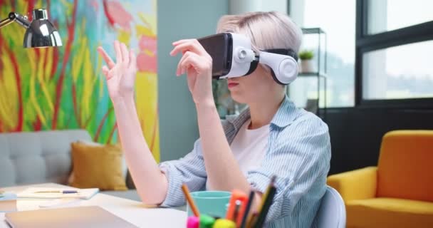 密切关注年轻的白种人妇女的肖像，她戴着VR眼镜，用现代技术在家中的办公桌前与空气握手。使用虚拟现实耳机的女性. — 图库视频影像