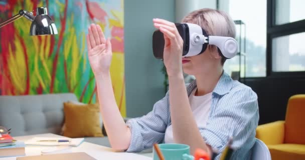 Närbild porträtt av unga kaukasiska blonda kvinnliga student i VR glasögon arbetar på projekt med modern teknik rulla i luften sitter i rummet hemma Kvinna arbetare med hjälp av virtuell verklighet headset — Stockvideo