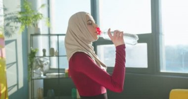 Spor yaptıktan sonra, güneşli oturma odasında durup gülümseyen bir gülümsemeyle kameraya bakan mutlu genç Arap kadının portresini yakından çek. Fitness, pozitif duygu konsepti