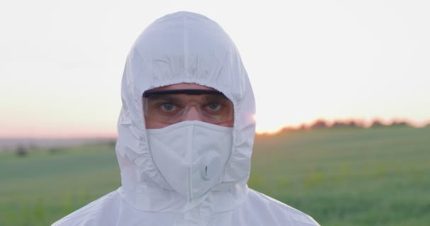 Portrait of caucasian farmer man wearing protective equipment looking at the camera at the field. Farmland sunset landscape agriculture. Farmland. Farmer fumigate in protective suit and mask. — Stock Video