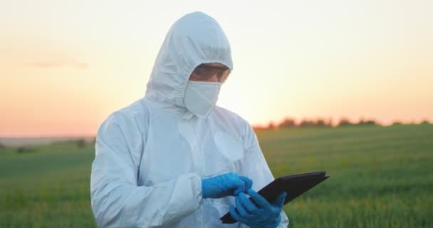 Male farmer expert wearing protective equipment browsing tablet computer applications while examining green crops at the field walking at the ecological organic farm garden — 비디오