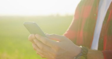 Ekose gömlekli iyimser beyaz çiftçi bilim adamının tarlada çalışırken akıllı cep telefonu teknolojisi uygulamasını kullanması ve gülümsemesi. Tarım kavramı
