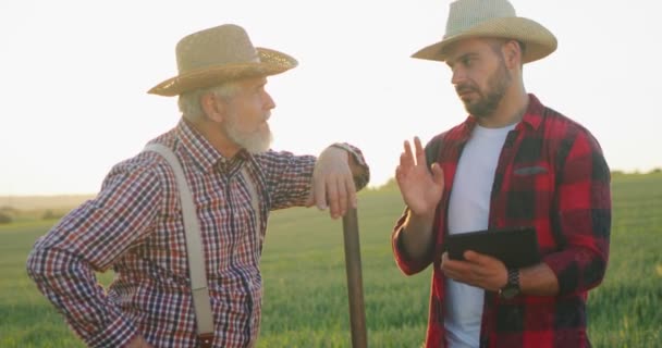 Digitaal apparaat in de landbouw. Senior boer ingenieur coaching stagiair in het monitoren van landbouwtechnologieën. Volwassen specialist vertelt iets aan zijn collega. Buiten het seizoen oogst en agronomie concept — Stockvideo