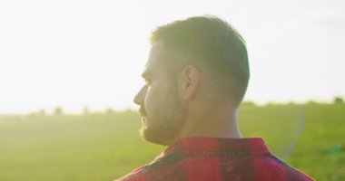 Çekici beyaz bir adamın portre resmi yeşil alanda duruyor, neşeyle gülümsüyor ve sahaya bakarken neşeli hissediyor. Yazın açık havada gülümseyen erkek çiftçi.