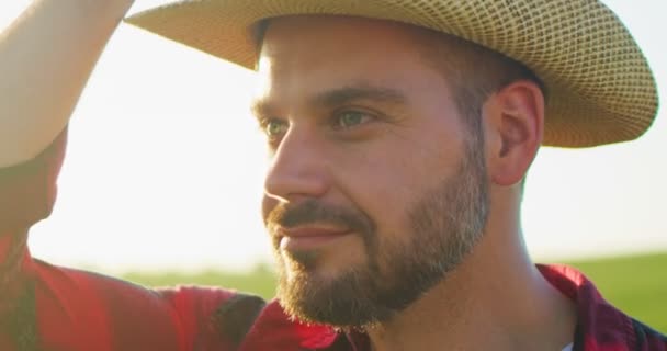 Retrato de agricultor adulto barbudo positivo usando chapéu permanecendo no plantio ou no campo e sorrindo para a câmera. Conceito de jardineiro, agronomia e agricultura — Vídeo de Stock