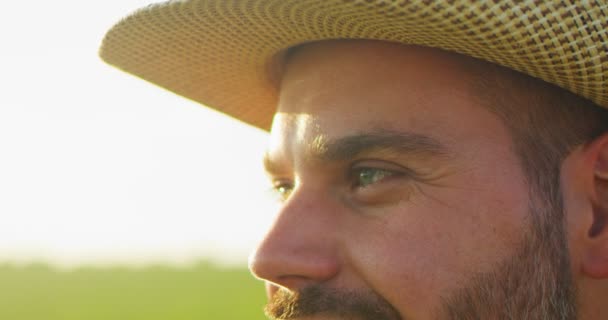 Cropped portrait of the thoughtful farmer looking away. Senior farmer smiling. Slow motion. Close up of the caucasian good looking young man with a beard smiling while looking at the field — 图库视频影像
