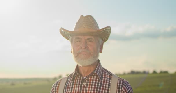 A figyelmes idősebb farmer portréja, amint a kamerába néz. Végzős farmer mosolyog. Lassú mozgás. Közelkép a kaukázusi kinézetű idős férfiról, szakállas mosollyal a kamerába. — Stock videók