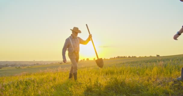 Hello. Full length view of the senior farmer giving handshake to his young colleague while working at the field at the sunset. Agricultural business concept — Stock Video