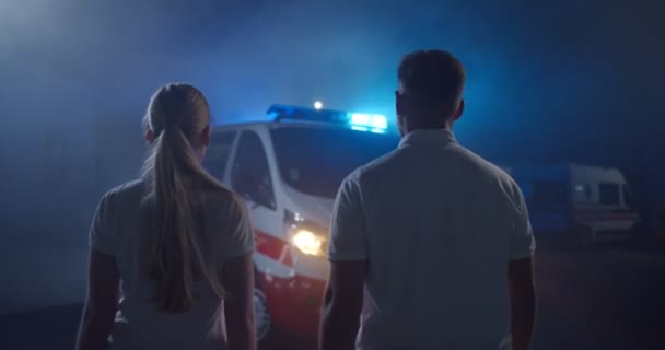 Trasera en un par de paramédicos caminando rápido al coche de la ambulancia en el turno de noche. Vista posterior de hombres y mujeres caucásicos médicos corriendo. Llamada de emergencia. Hombres y mujeres colegas enfermeras. — Vídeo de stock