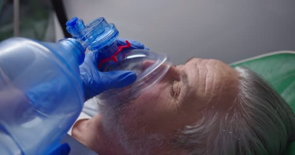 Primer plano de enfermo o herido en accidente anciano en ambulancia con máscara para respirar. Paciente masculino con coronavirus en respiración hospitalaria con oxígeno. Primeros auxilios. Paramédico con máscara. Trabajo paramédico. — Vídeo de stock