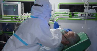 Şahsi koruyucu ekipman sağlıkçısı ambulanstaki ihtiyarın hayatını kurtardı. Sıhhiye hastaya oksijen veriyor ve göz tepkisini kontrol ediyor. Reanimasyon. Covid sırasında tıbbi işler. Doktorun ilk yardımı. PPE.