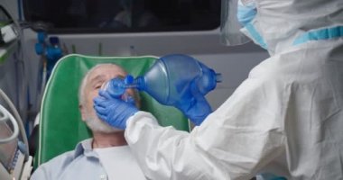 Özel koruma ekipmanlarında doktor sağlık görevlisi ambulansta yaşlı adamın hayatını koronavirüsten kurtarıyor. Sıhhiye hastaya oksijen veriyor. Reanimasyon. Covid-19 sırasında tıbbi işler. İlk yardım. PPE.