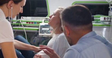 Ambulansta doğururken nefes alıp veren beyaz bir kadın yorulmuştu. Ebe ve koca destekçisi. Doğum sancısı çeken bir kadın hastaneye giderken bağırıyor..