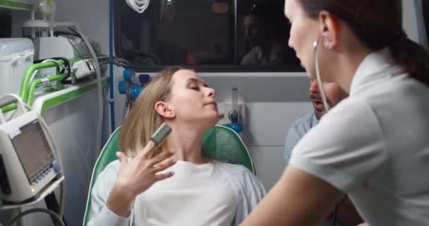 Caucasian beautiful woman in pain breathing hard and pushing when in labor and handsome husband supporting her while holding hand. Midwife in stethoscope listening heartbeat and helping in ambulance. — Stock Video