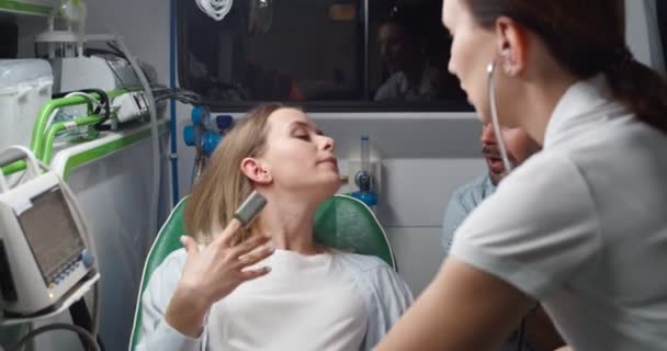 Blanke mooie vrouw met pijn die hard ademt en duwt als ze weeën heeft en knappe man die haar steunt terwijl ze hand in hand houdt. Vroedvrouw in stethoscoop luisteren hartslag en helpen in ambulance. — Stockvideo