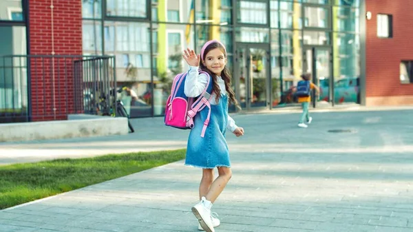 Söt liten flicka med rosa ryggsäck som springer på skolgården och ler. Vackra glada små kvinnliga junior elev gooing till skolan på gott humör. Elever som springer till lektionerna. Studie, skolkoncept — Stockfoto