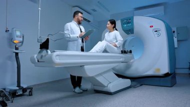MRI kapsülü ve klinikte yeni modern ekipmanlar. Modern klinikte biyopsi için röntgen bekleyen Asyalı kadın hasta. Tarayıcı masasında otururken doktoruna mide ağrısı şikayeti..