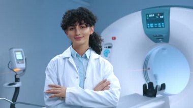 Kafkas tomografi uzmanı çapraz kollarla poz veriyor. Tomografinin arka planında gülümseyen doktor. MRI incelemesi için modern donanımlı oda. MRI kapsülü. MRI uzmanı. Sağlık çalışanı.
