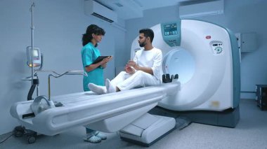 Tıbbi tesisler, modern teknoloji ve MR makinesi. Modern klinikteki tarama masasında oturan hasta, doktorların biyopsi ve sağlık hizmetlerinin röntgen incelemesi hakkında açıklamalarını dinliyor..