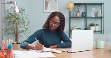 Çok güzel bir Afro-Amerikan öğrencinin portresi dizüstü bilgisayarında video dersi alırken masada oturup planlama notları alırken. Bilgisayarda kadın konuşmaları ve yazılar