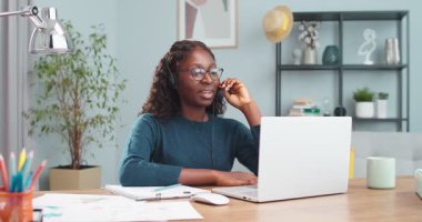 Güzel Afro-Amerikan kız öğrencinin portresi. Kulaklık takmış, masada oturmuş konuşurken dizüstü bilgisayarında video dersi alıyor. Kız bilgisayarda görüntülü konuşuyor. Konsept çalış
