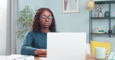 Evdeki masada otururken dizüstü bilgisayarında yazı yazan çok güzel bir genç kadının portresi. Bilgisayarda gezinen ve rahat bir odada çalışan güzel Afrikalı Amerikalı kadın işçiler. Görev konsepti