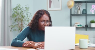 Mutsuz, Afro-Amerikan güzel kız işçi masa başında otururken dizüstü bilgisayara bakıyor. Modern kabinede hayal kırıklığına uğramış, üzgün, serbest çalışan kadın portresi. Duygular konsepti