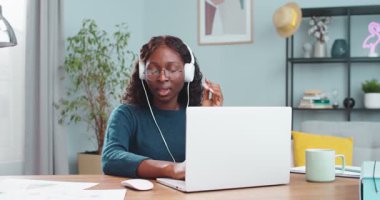 Masasında oturmuş kulaklıkla müzik dinlerken dizüstü bilgisayarda yazan neşeli Afro-Amerikalı güzel kız. Bilgisayarda gezinen serbest kadın portresi. Kapalı alan kavramı