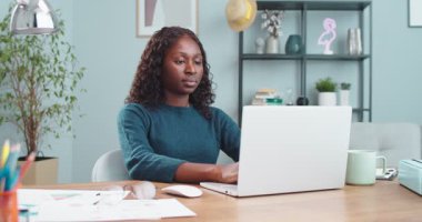 Genç, güzel, mutlu, Afro-Amerikan bir bayan masada oturuyor ve bilgisayarın içinde interneti arıyor. Neşeli bir kızın portresi dizüstü bilgisayarı kapatıp oturma odasında tek başına gülümsemesi. Boş zaman konsepti