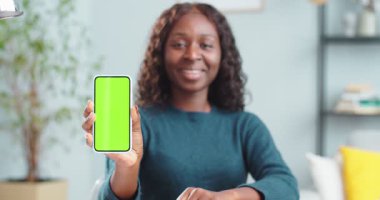 Güzel, Afro-Amerikan kıvırcık kız portresi. Elinde yeşil ekranlı akıllı telefon, içeride gülümsüyor. Elinde krom anahtarı olan, cep telefonu olan güzel bir kadın. Teknoloji konsepti