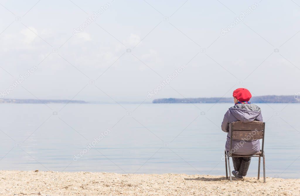 Elderly woman admires sea view on a beach in sunny day. Travel concept. Loneliness concept.